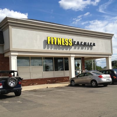 Exterior view of fitness premier gym with large yellow signage above the entrance, under a blue sky.