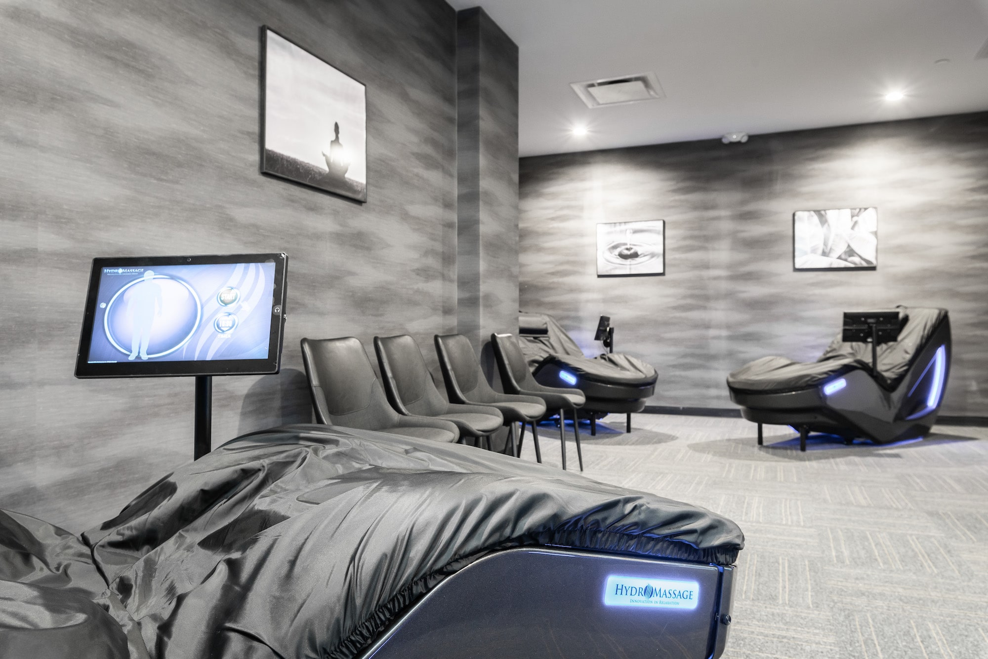 Modern spa lounge with massage chairs and framed wall art, featuring gray decor and a relaxing ambiance.