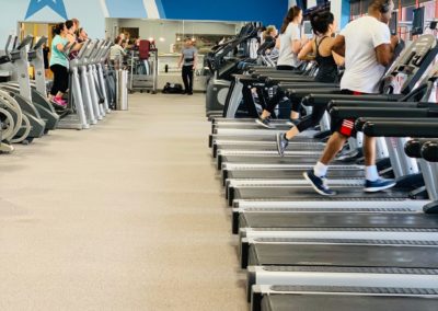 People exercising on treadmills in a gym with exercise equipment and televisions.