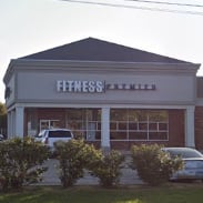 Exterior view of a fitness center building with a clear sign labeled "fitness" and parked cars in front.