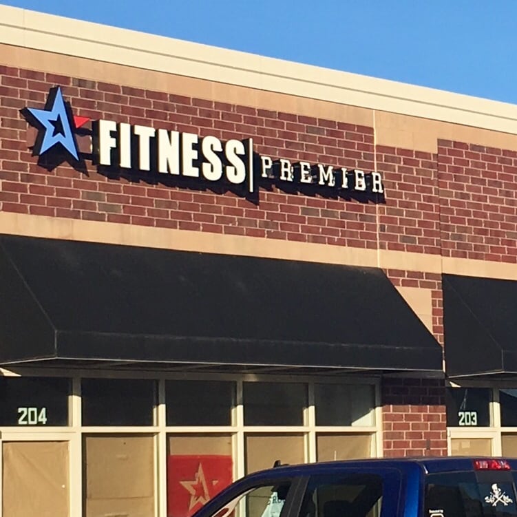 Sign reading "fitness premier" with a star logo on a brick building façade, with a blue truck parked in front.