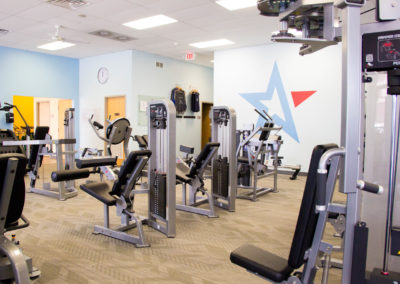Modern gym interior featuring various exercise machines including treadmills and weight stations with a blue and gray color scheme.