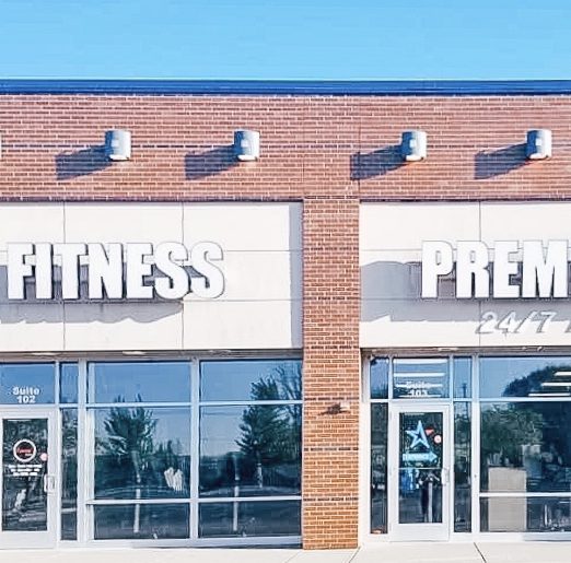 Exterior view of a fitness center with large, clear windows and bold signage under a clear blue sky.