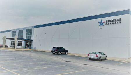 Exterior of a large premier fitness gym building with a blue and white facade and two cars parked in front.