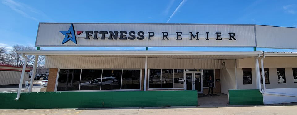 Exterior of fitness premier gym with a large sign above the entrance, featuring a star symbol under a clear blue sky.