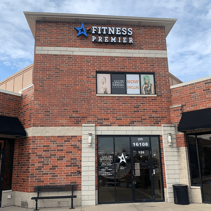 The exterior of a brick building features signage for 'fitness premier' above a salon advertisement under a clear sky.