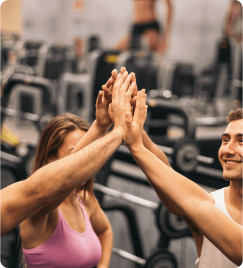 Three individuals high-five each other at a gym. Exercise equipment is visible in the background.