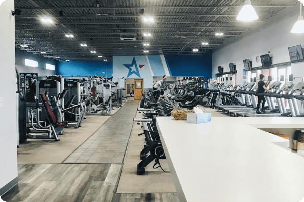 Spacious gym interior with various exercise machines and treadmills. High ceiling, bright lighting, and a few people working out.