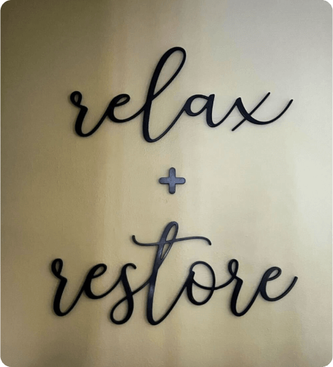 Wall art with the words "relax + restore" in cursive letters on a plain background.